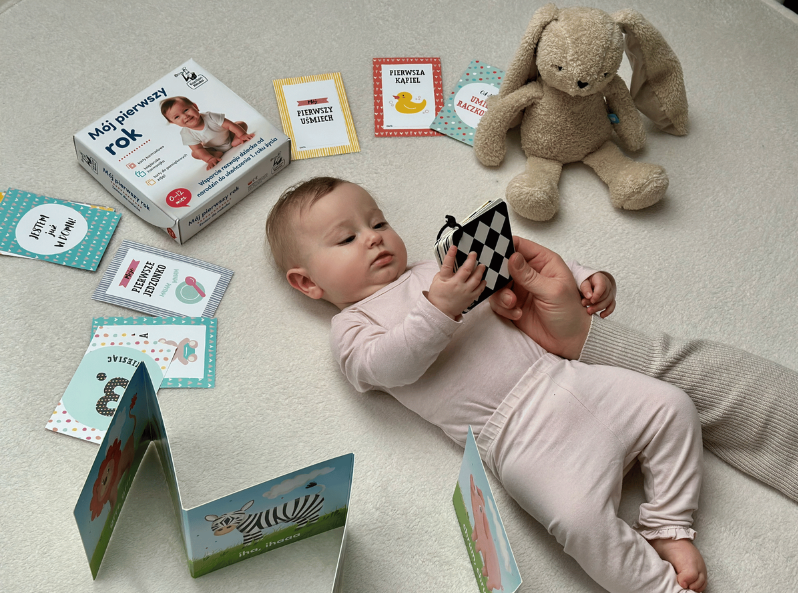 Maluch patrzy na karty kontrastowe z zestawu Mój pierwszy rok, wokół karty pamiątkowe oraz książeczka-harmonijka