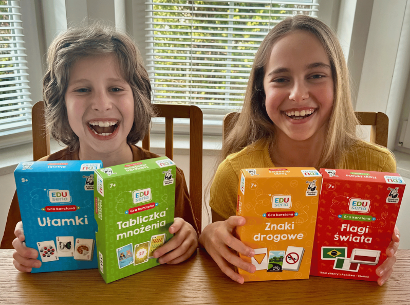 Gry karciane EDUseria od Kapitana Nauki – wesołe dzieci trzymają produkty edukacyjne dla uczniów