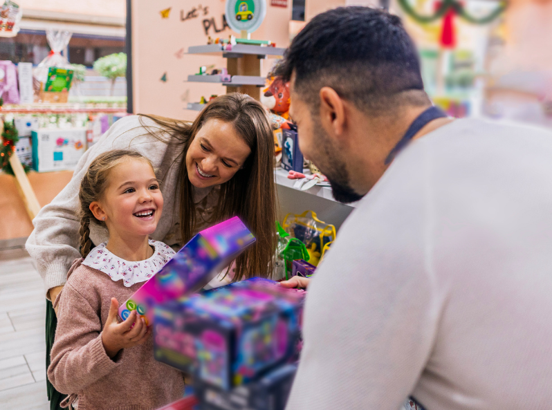 uśmiechnięta dziewczynka i jej mama rozmawiają z ekspedientem