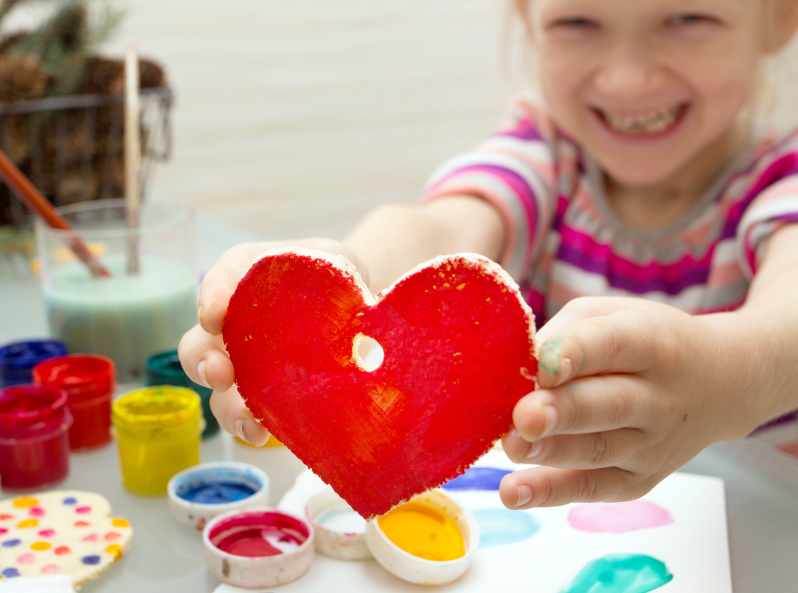 Dziewczynka tworzy serduszko z masy solnej i maluje je farbami