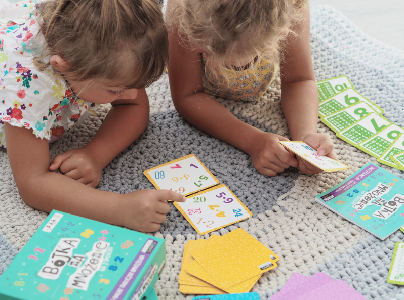 Dzieci grające w karty edukacyjne z gry Bójka na mnożenie pokazujące działania matematyczne i wyniki