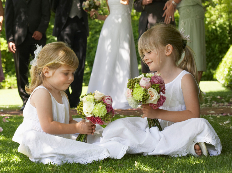 dwie dziewczynki w weselnych strojach bawią się na trawie