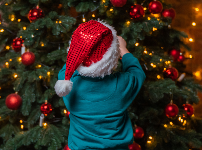 Dziecko stoi tyłem i wiesza bombkę na choince.