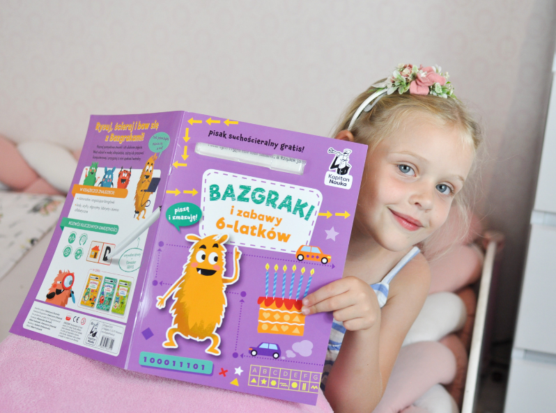 Szczęśliwa dziewczynka trzyma książkę Bazgraki i zabawy 6-latków