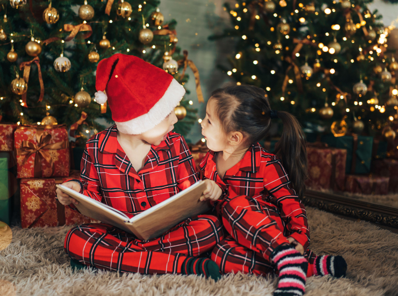 Dzieci siedzą pod choinką i czytają książkę.