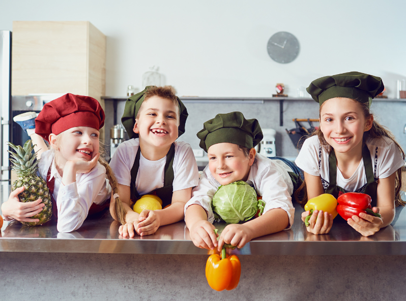 dzieci w kuchni radośnie trzymają warzywa i owoce