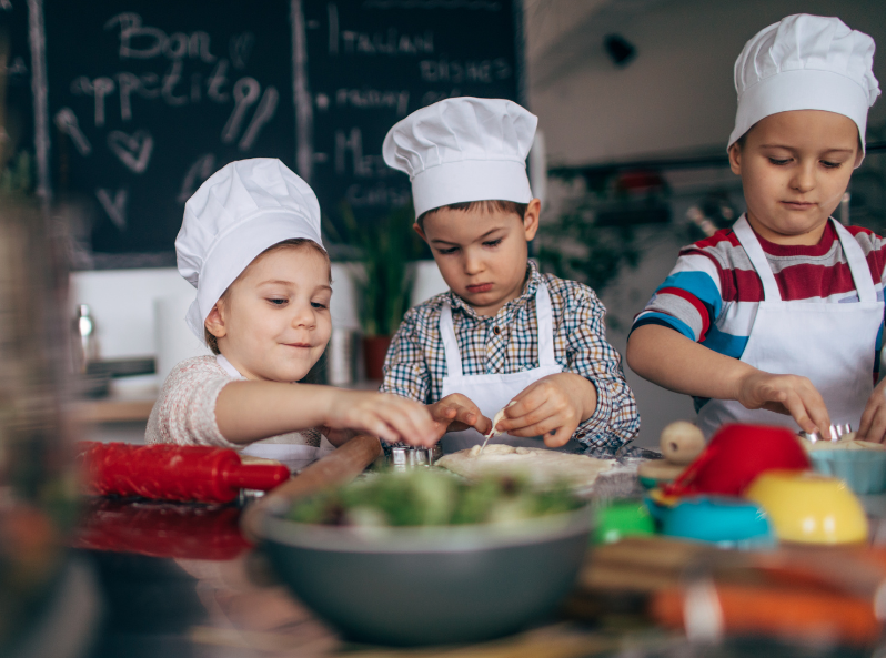 troje chłopców, w czapkach kucharzy, w skupieniu przygotowuje posiłek w kuchni